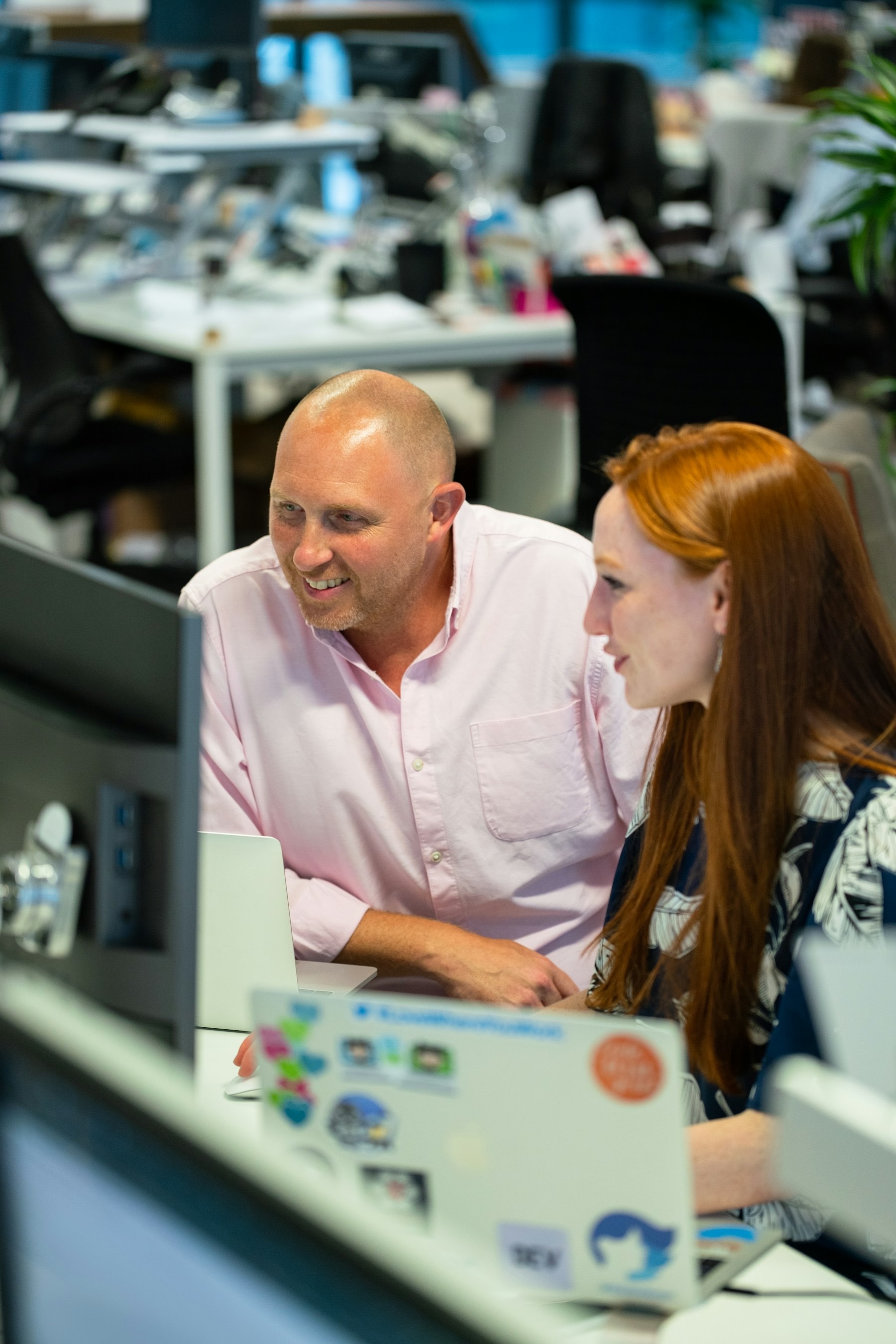 Two colleagues reviewing work on a monitor in an open-plan office